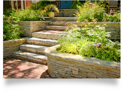 Natural stone steps lead up through landscaped raised beds (or terraced gardens), bordered with natural stone walls to create a beautiful transformation for this quiet corner.